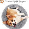 A light brown and white dog is lying on a gray plush round pet bed.