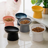 A collection of ceramic pet bowls in various shades of gray, black, and white are displayed on a light surface next to a whit