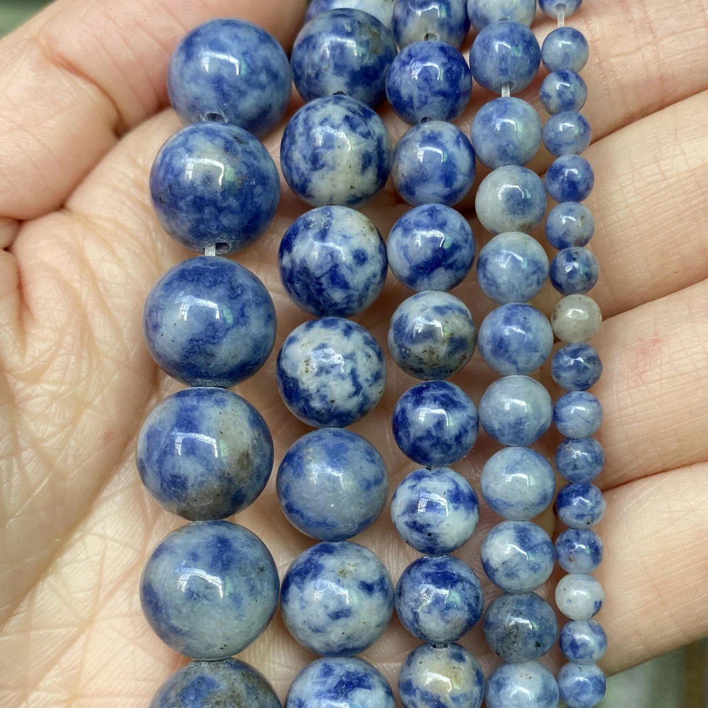 A hand holds a strand of blue and gray natural stone beads for jewelry making