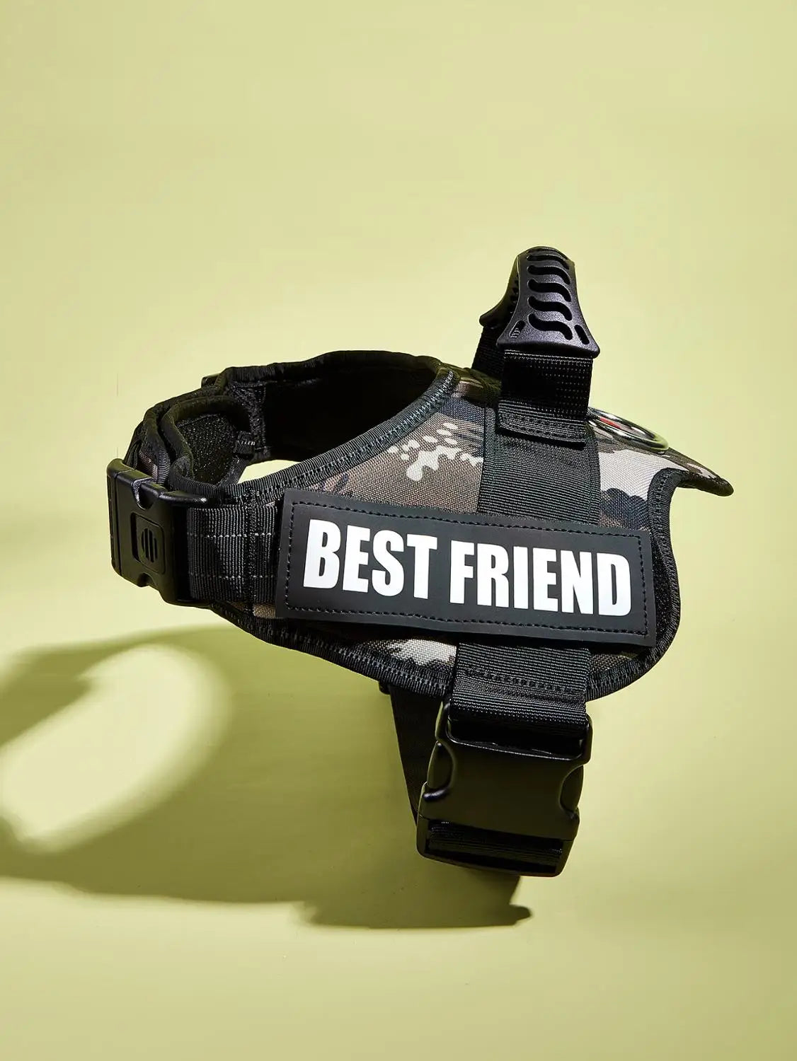 Black dog harness vest with a white Best Friend rectangular tag and reflective stripes against a light green background.