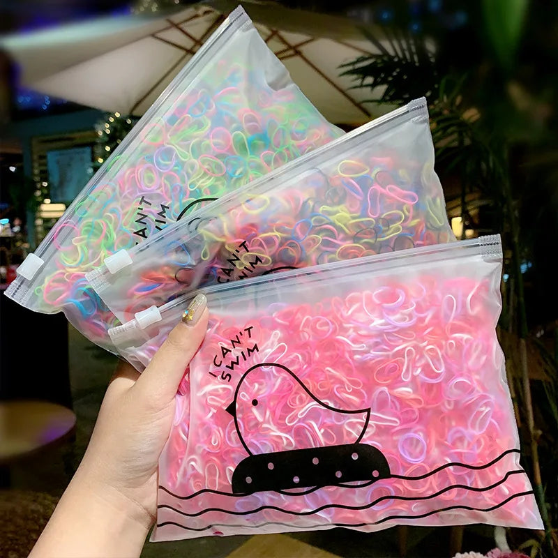 Eine Hand hält einen durchsichtigen Plastiksack mit farbenfrohen Gummibändchen für Mädchen