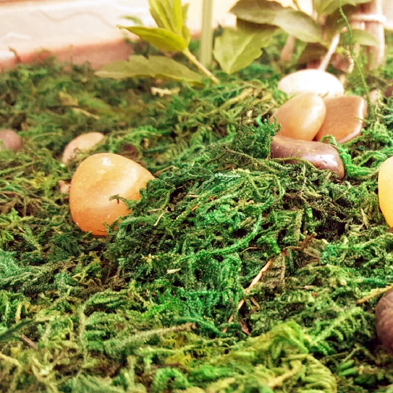 A close-up of artificial green moss with smooth, amber and brown stones used for crafts and decor.