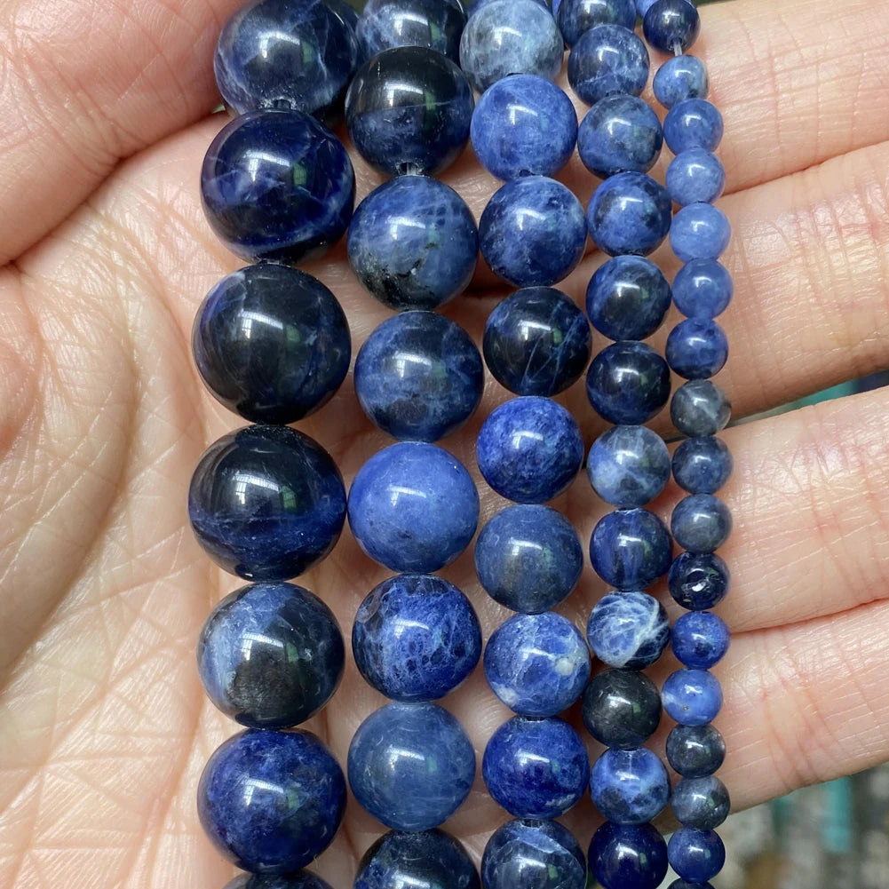 A hand holds a strand of dark blue and purple natural stone beads for jewelry making.
