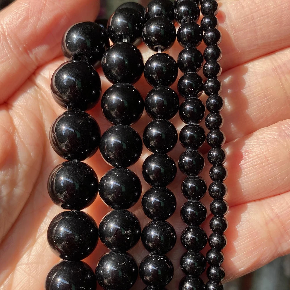 A hand holds multiple strands of black natural stone beads for jewelry making