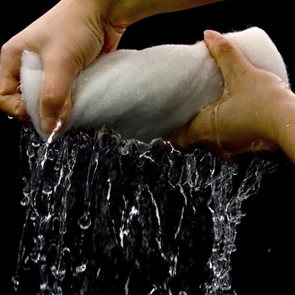 Hands are rinsing a white dual-density aquarium filter sponge under running water.