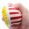 A hand holds a white squishy toy shaped like a popcorn bucket with red and yellow stripes.