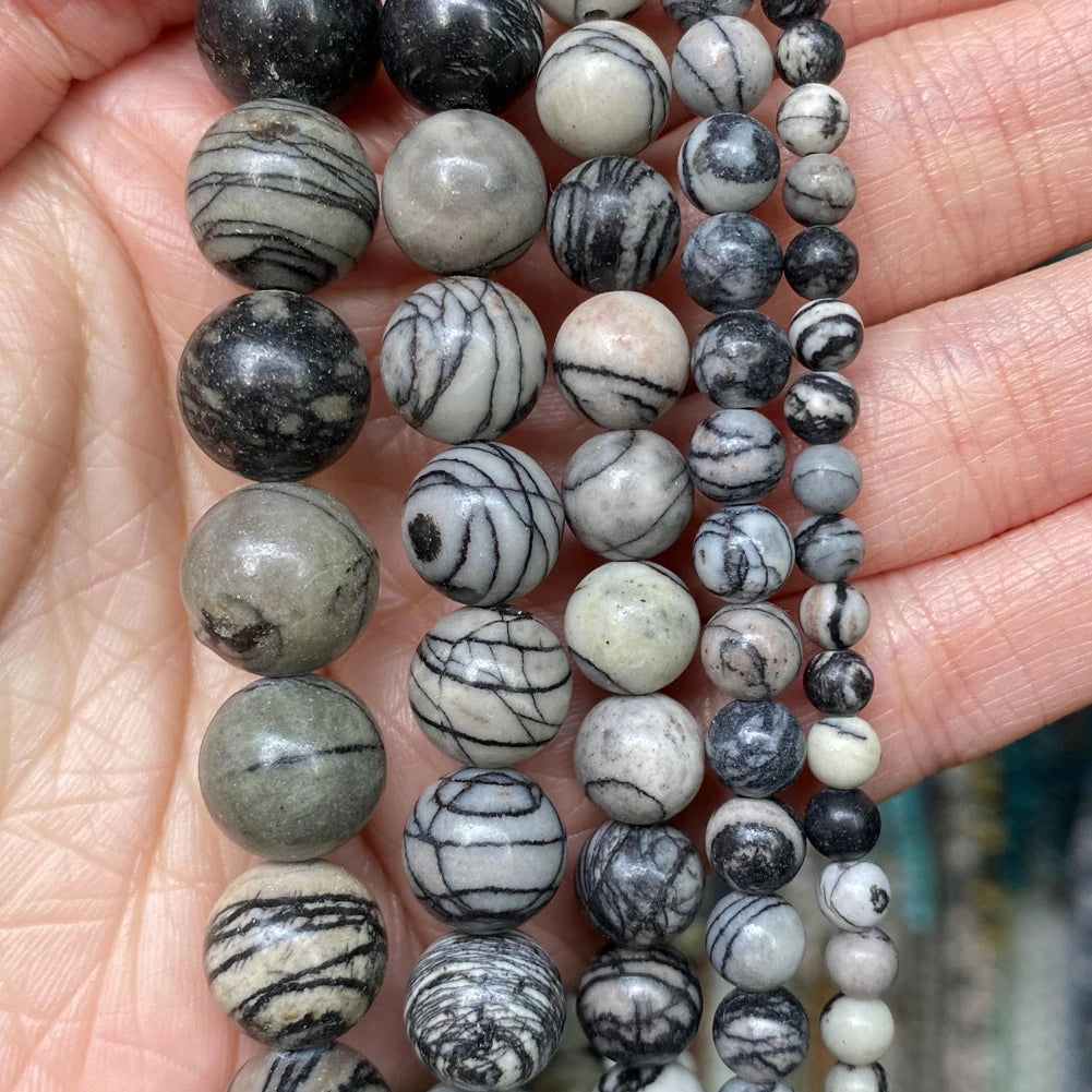 A string of natural stone beads in various shades of gray, black, and white is displayed on a hand.