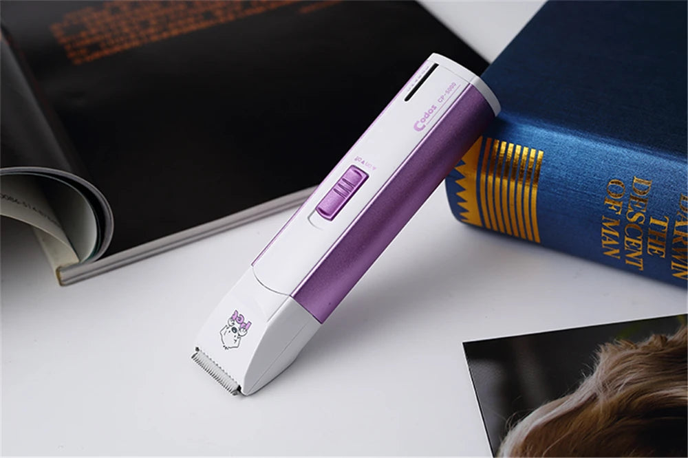 A purple and white electric pet grooming clipper is shown next to a book on a white surface.