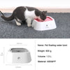 Un chat noir et blanc boit de l'eau dans un bol flottant blanc sur une surface de tissu grise.