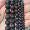 A string of black natural stone beads for jewelry making, showing various sizes and textures.