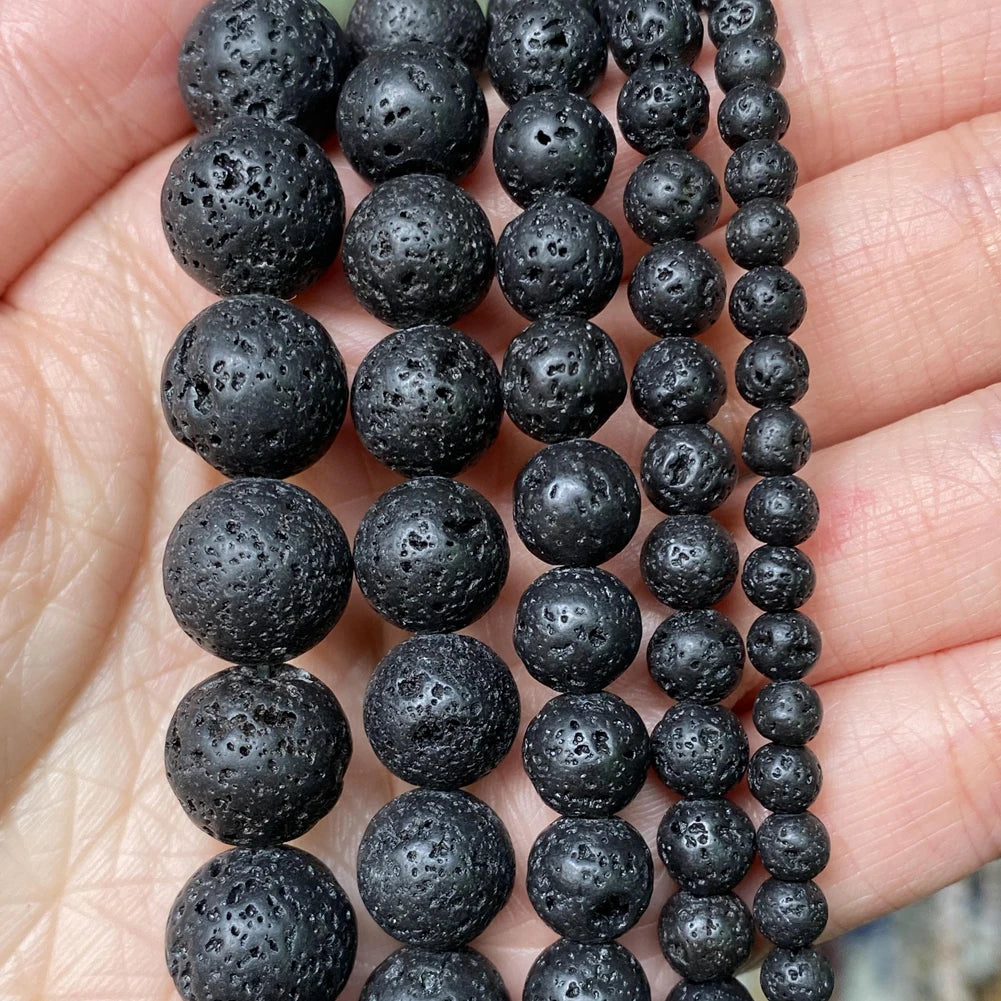 A string of black natural stone beads for jewelry making, showing various sizes and textures.