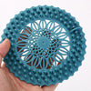 A hand holds a flexible silicone drain cover with a handle, featuring a circular, flower-like pattern for hair and debris.