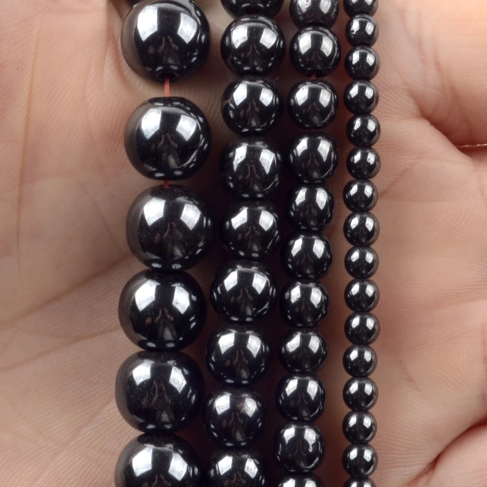 A hand holds a strand of black polished natural stone beads for jewelry making.