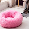 A fluffy pink round pet bed with an anti-slip base resting on a light wooden floor.