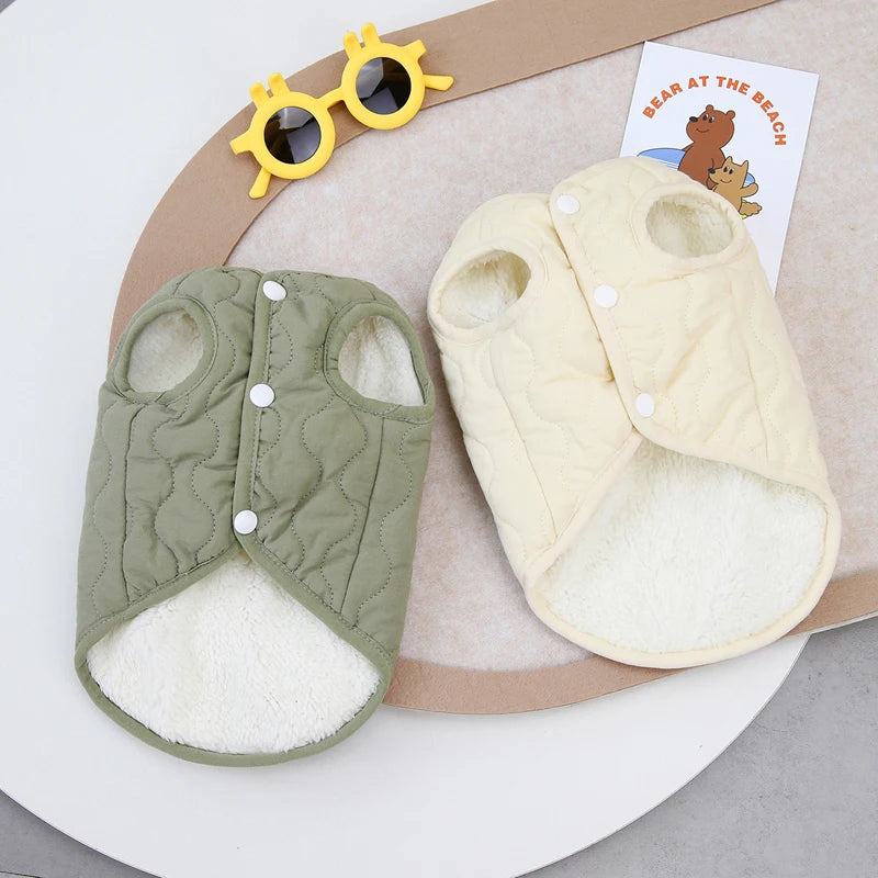 A light yellow quilted pet vest with a fuzzy lining is displayed next to sunglasses and a card.