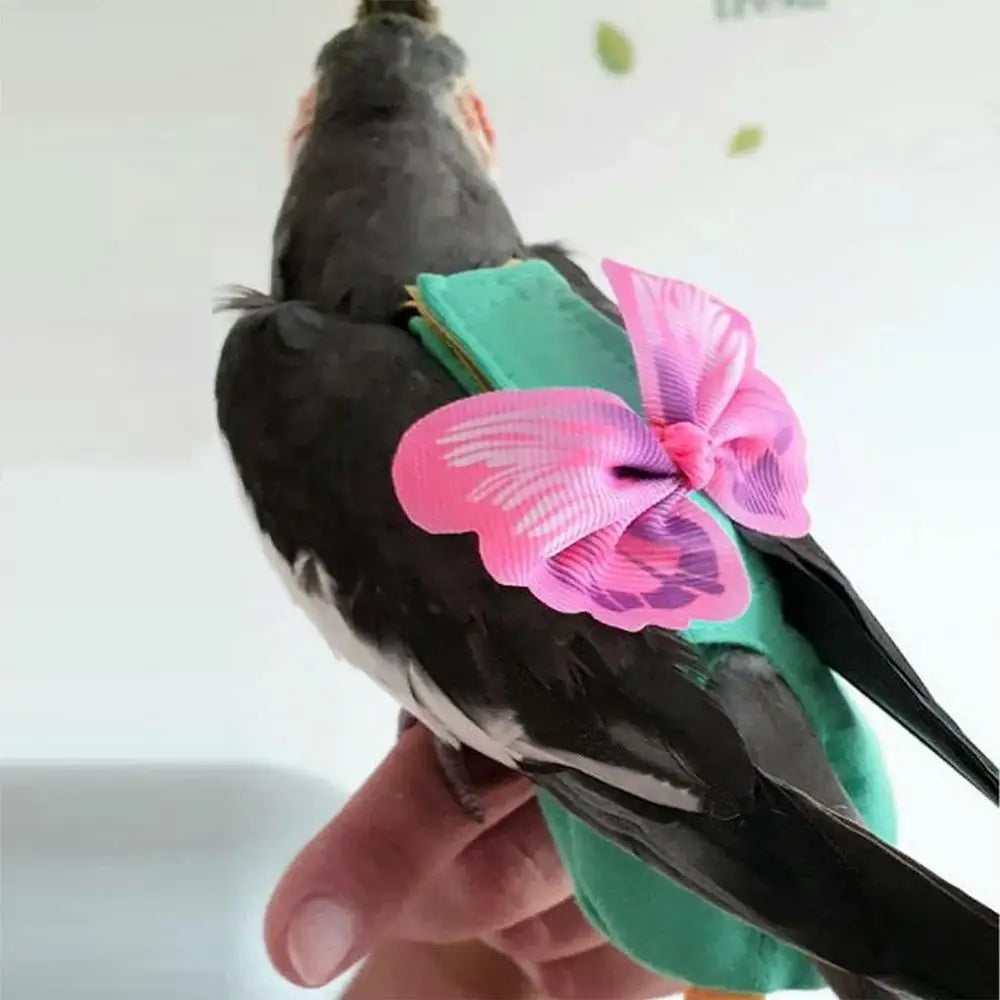 A hand holds a black parrot wearing a pink floral flight suit with green accents.