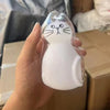 Klare Silikonkatze mit schwarzen Schnurrhaaren und Augen wird in einer Hand vor einem Kartonkarton präsentiert.