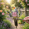 A yellow and gray parrot perched on a stick in a garden setting.