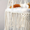 An orange and white cat is sleeping on a fluffy white hammock bed made of macrame fibers.
