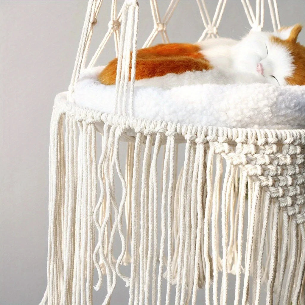 An orange and white cat is sleeping on a fluffy white hammock bed made of macrame fibers.
