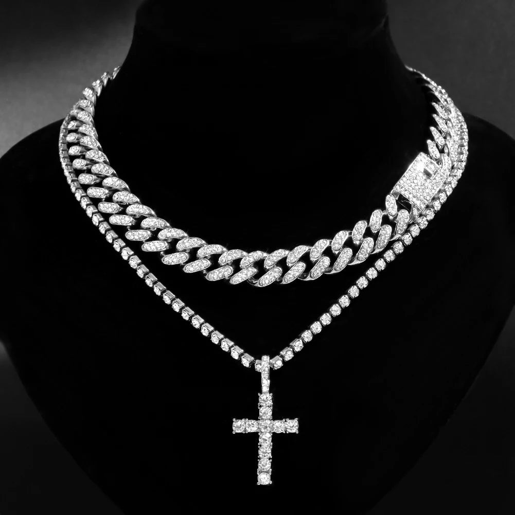A close-up of a dainty diamond Cuban link necklace set featuring a layered chain and a cross pendant.