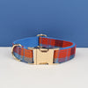 A plaid dog collar in blue and orange fabric with a gold-toned buckle resting on a white surface.
