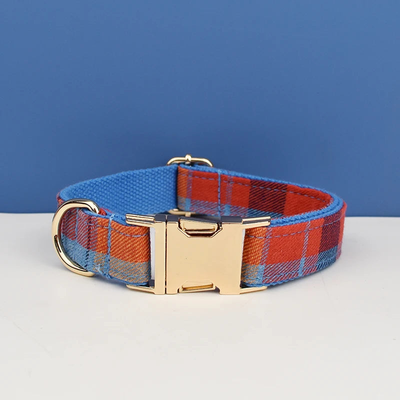 A plaid dog collar in blue and orange fabric with a gold-toned buckle resting on a white surface.