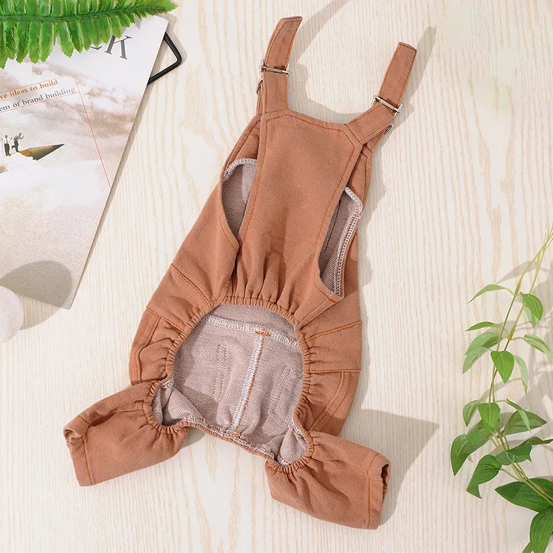A tan dog denim jumpsuit costume for small to medium breeds lying on a light wooden surface.