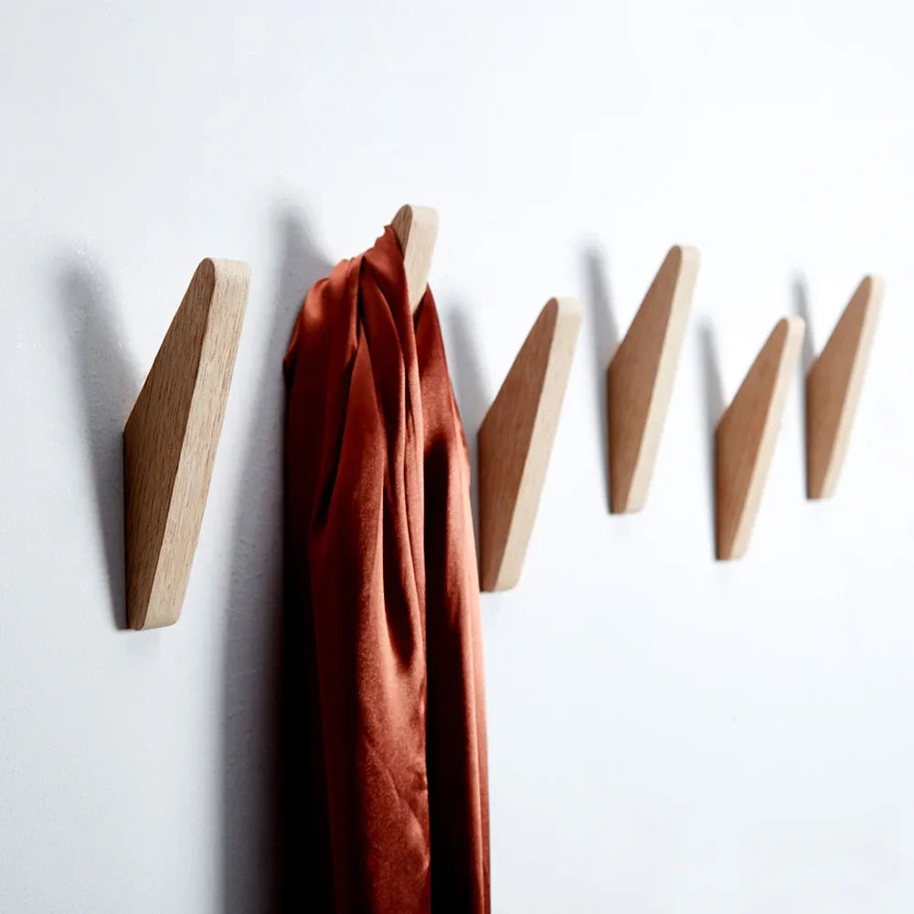 A set of three oak wood wall mounted triangle coat hooks in a burnt orange fabric hanging against a white background.