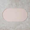 A rectangular, light pink non-slip feeding mat placed on a textured gray surface.