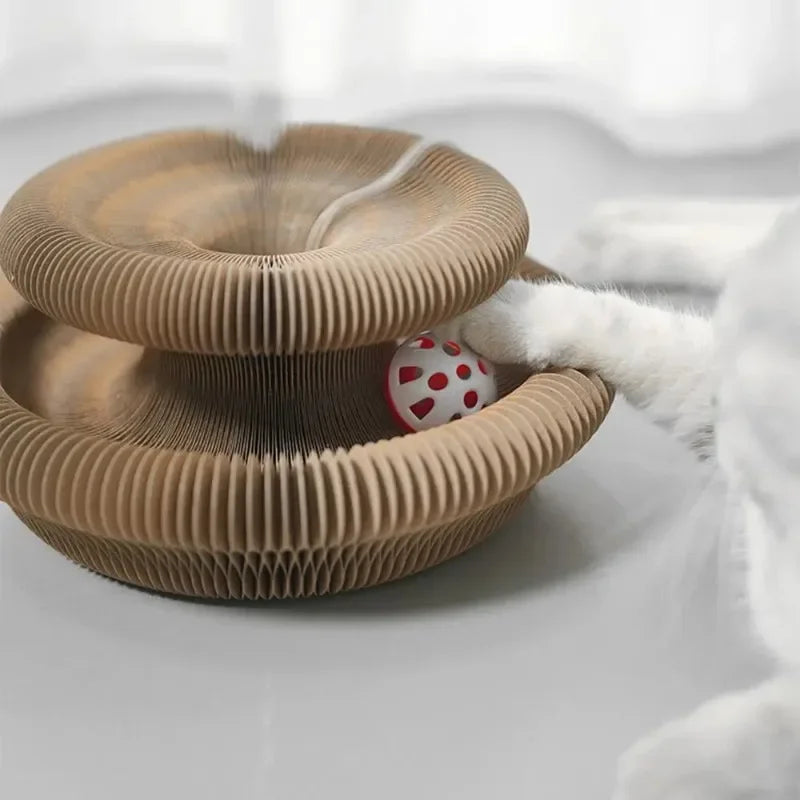 A round, brown accordion-style scratching board with a small red and white ball is shown on a white surface.