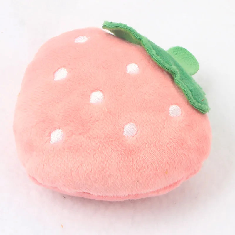 A pink strawberry shaped squeaky plush dog toy with green leaves and white dots.