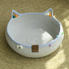 A light gray cat scratcher and comfort bed with a woven texture and colorful play balls.