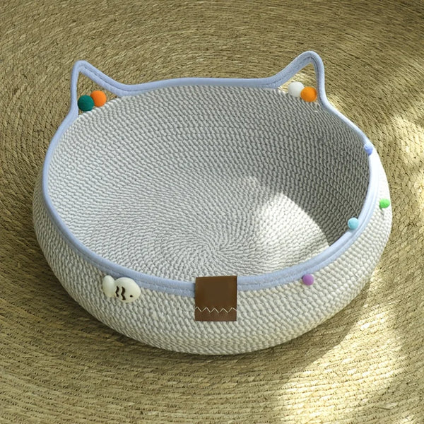 A light gray cat scratcher and comfort bed with a woven texture and colorful play balls.