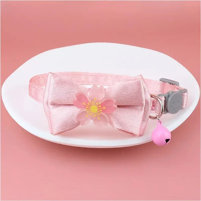 Pink lace bow cat collar with a bell and a pink bead charm displayed on a white plate.
