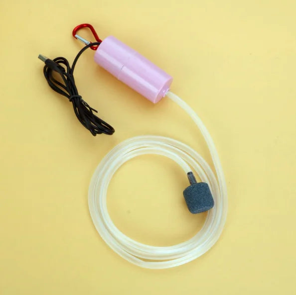 A portable USB aquarium oxygen pump with a pink connector and white tubing is shown on a yellow background.