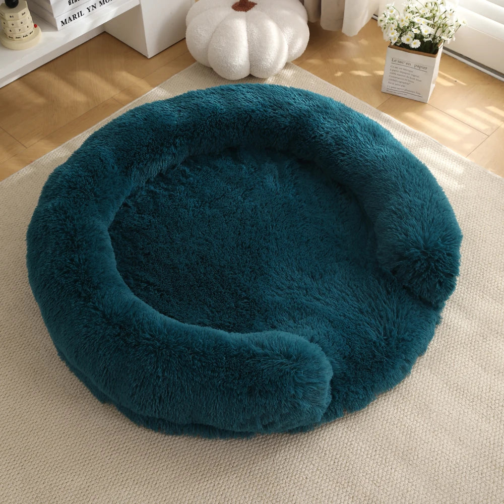 A round, deep teal faux fur dog bed resting on a light beige rug.