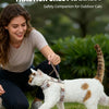 A woman is holding a cat wearing an escape-proof chest harness outdoors.