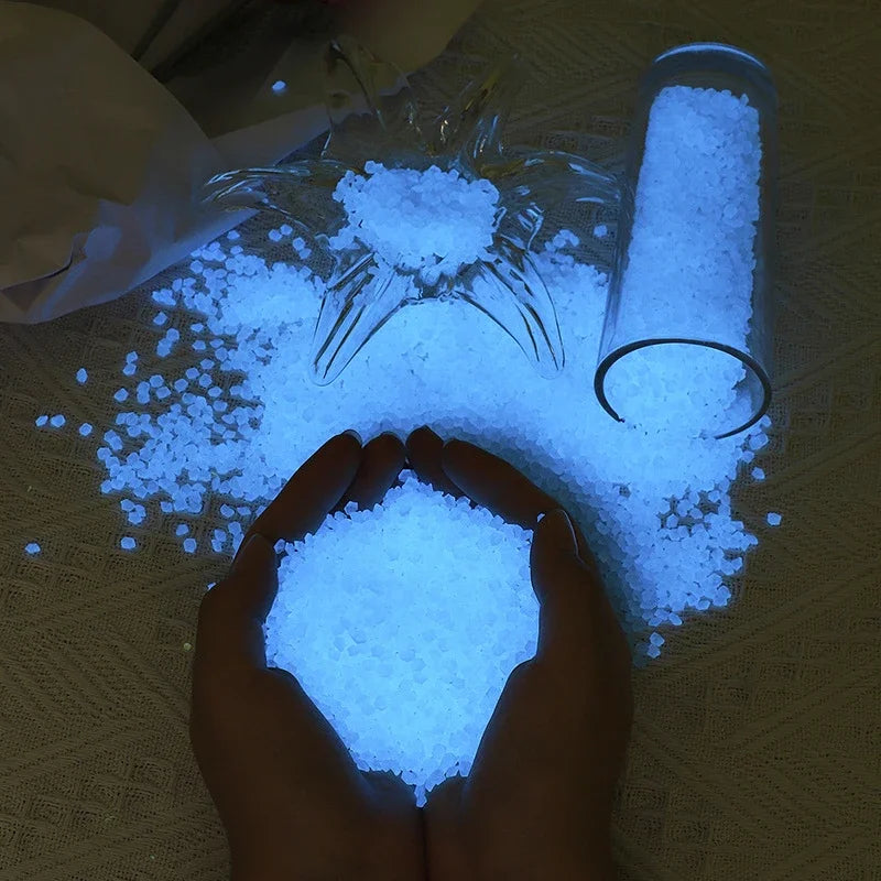 Hands holding glowing blue glow-in-the-dark decorative pebbles scattered on a surface.