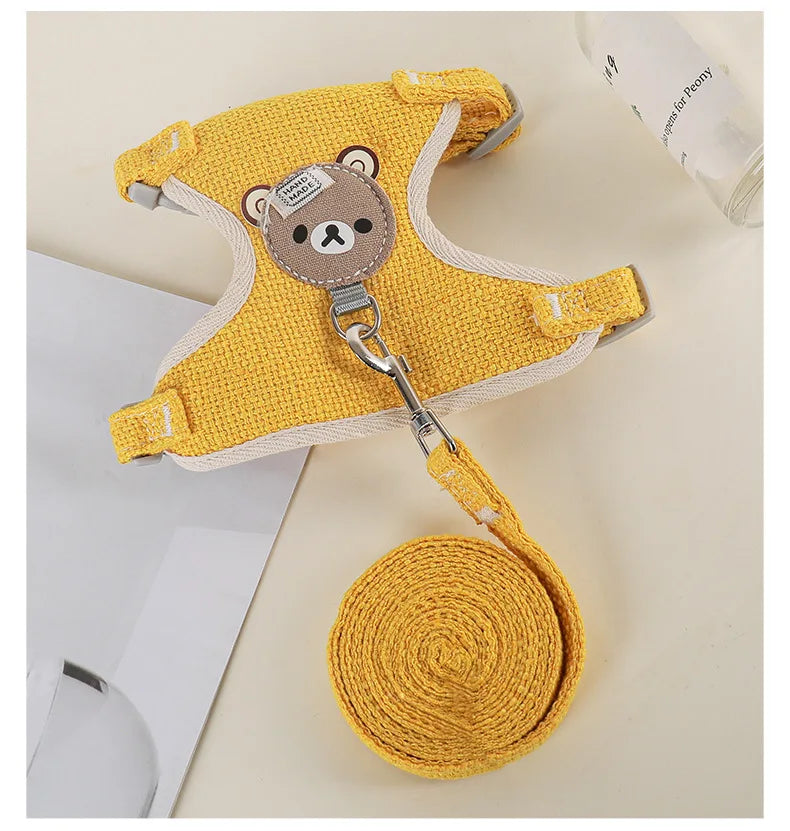 A yellow nylon dog harness with a bear charm and a matching yellow coiled leash is displayed on a light surface.