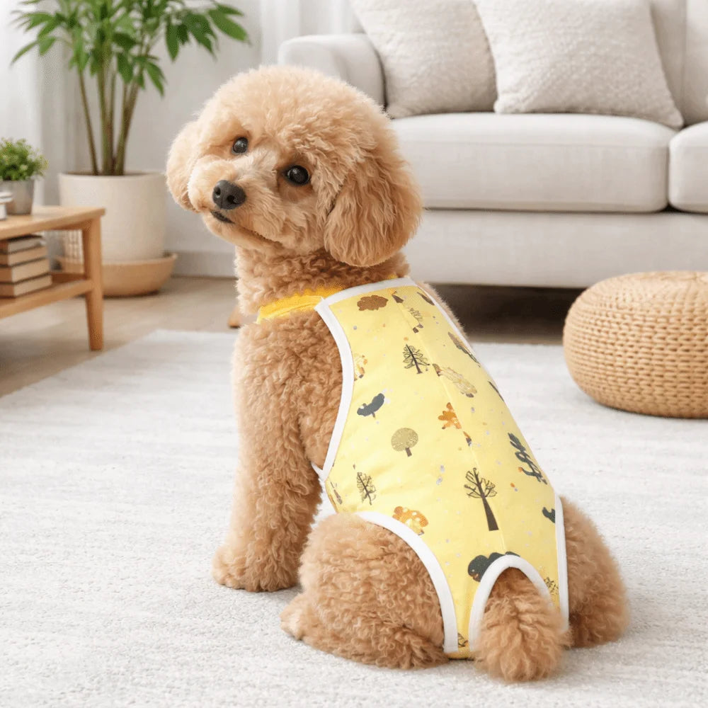 A fluffy light brown dog wearing a yellow reusable adjustable diaper with a shoulder strap, sitting on a white rug.