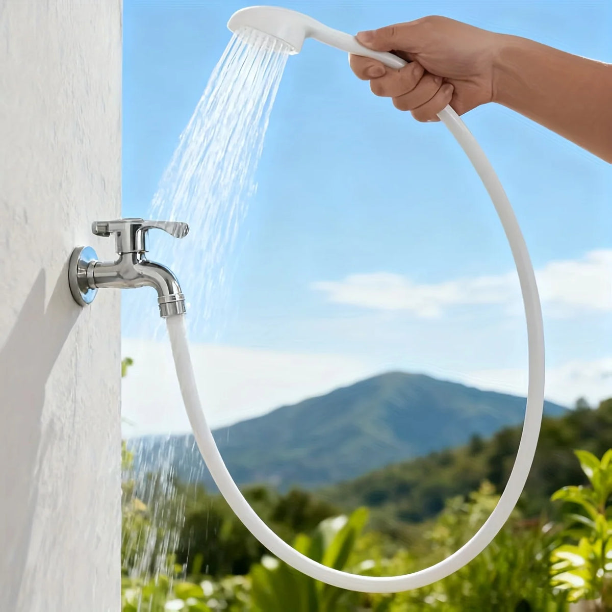 A hand is using a white 360° portable faucet sprayer with a long hose to spray water onto a white wall.