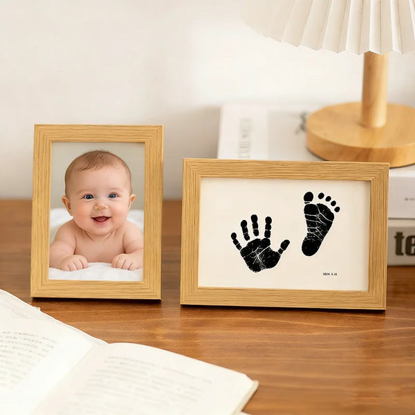 A framed print showing a baby's handprint and footprint on white paper, displayed on a wooden table.