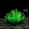 A dense, bright green artificial aquatic plant cluster with small pink flowers is shown on a dark gravel surface.