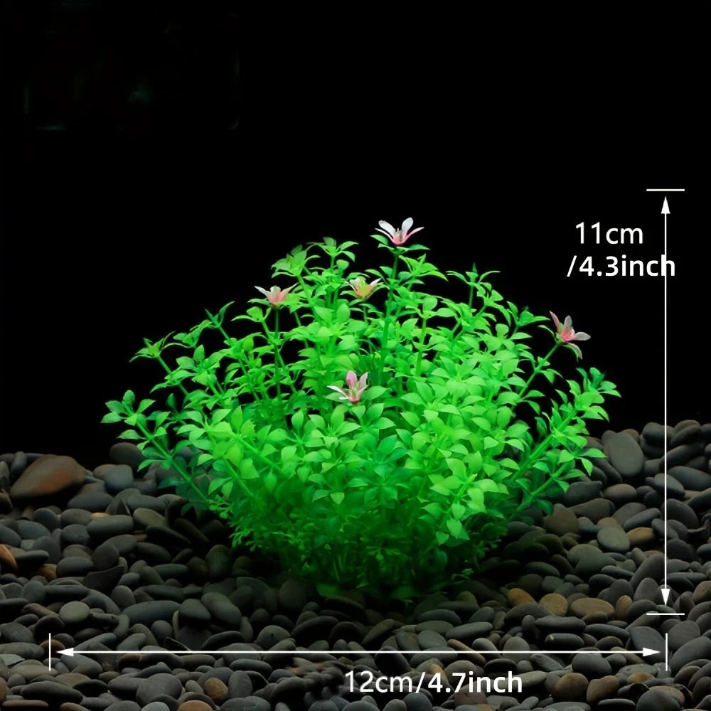 A dense, bright green artificial aquatic plant cluster with small pink flowers is shown on a dark gravel surface.