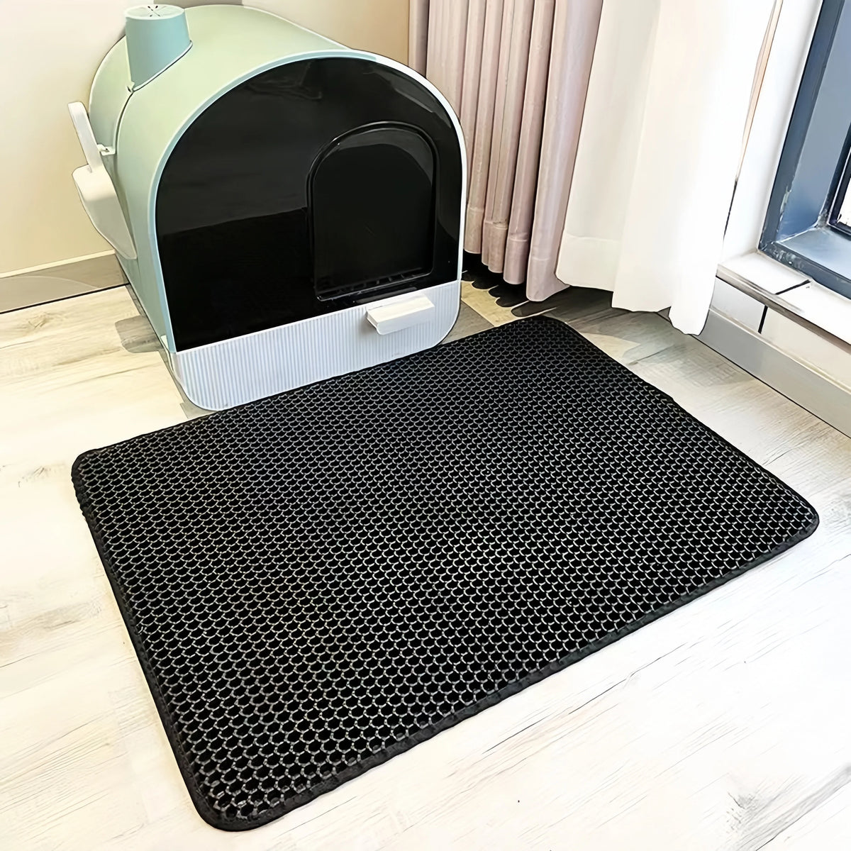 A black double-layer EVA cat litter mat is placed on a light wooden floor next to a light green pet enclosure.