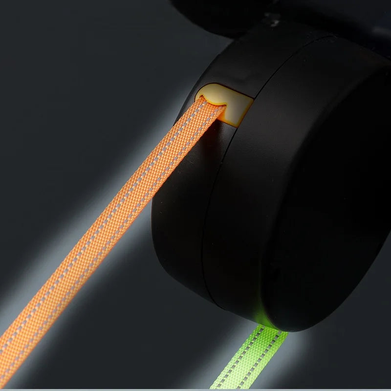 A close-up view of a retractable dog leash with an orange cord and a green strap, showing the mechanism.