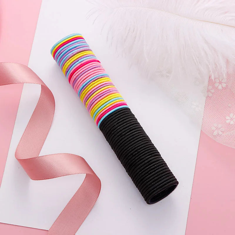 Una pila de bandas para el pelo elásticas de colores con rayas variadas y una banda negra sobre papel blanco con accesorios r