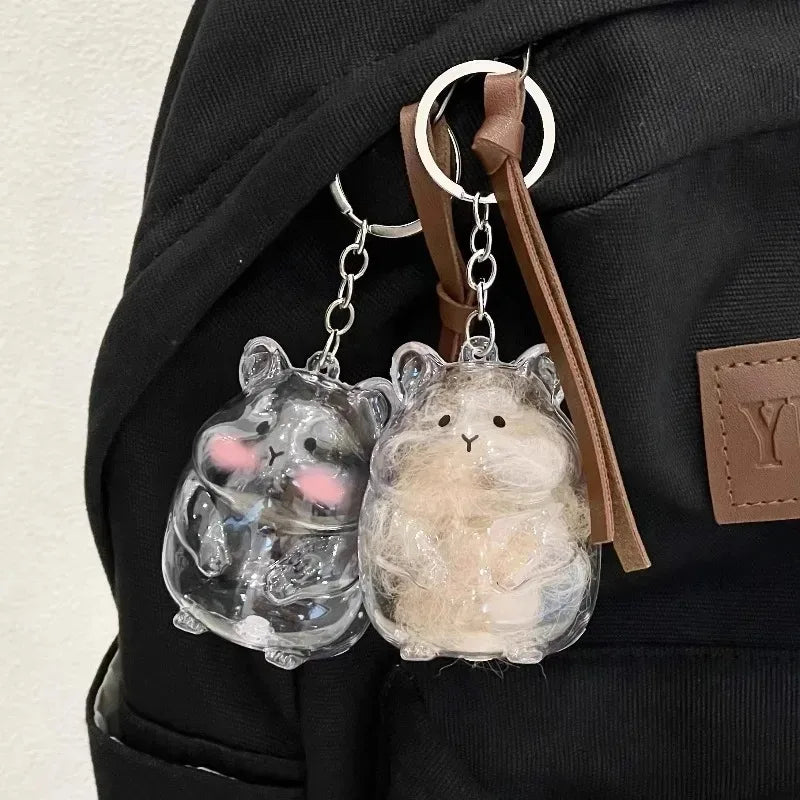 A clear glass hamster figurine with pink accents hangs from a leather keychain on a black fabric background.