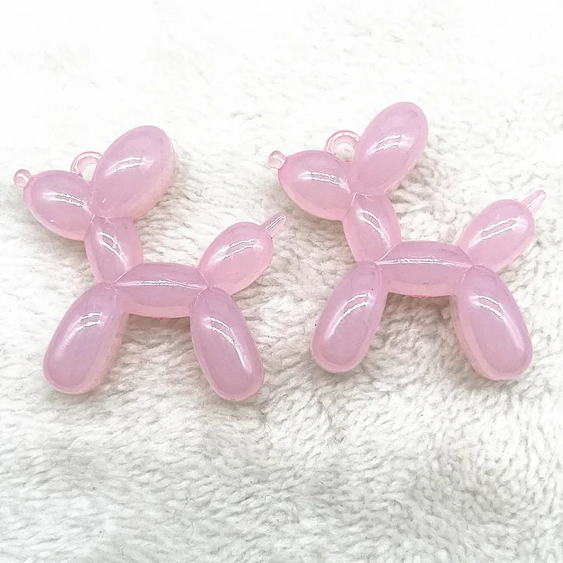Two pink acrylic balloon dog charm pendants displayed on a white, fuzzy surface.